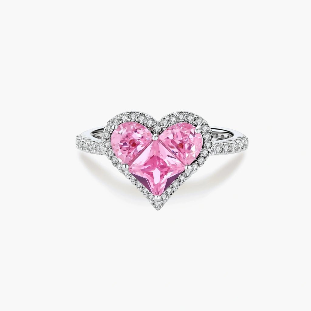 Heart-shaped ring with pink zirconia stones in white gold-plated setting, adjustable band on neutral background.